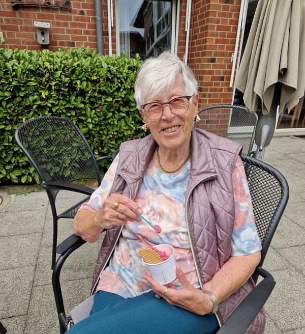 Eine Frau hält einen Becher mit Eis in der Hand und lächelt in die Kamera.