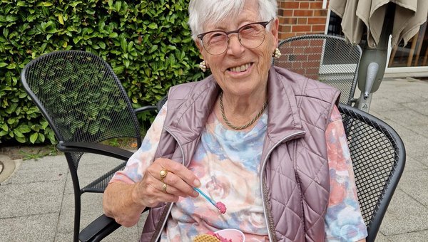 Eine Frau hält einen Becher mit Eis in der Hand und lächelt in die Kamera.