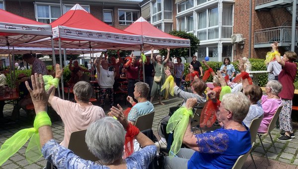 Man blickt über eine Gruppe Senioren, die einen Sitztanz vorführen, ihnen gegenüber steht Publikum, das mitmacht.