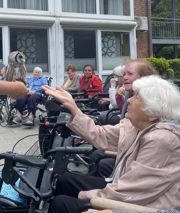 Eine Seniorin begegnet einem Kauz aus nächster Nähe und hält ihm ihre Hand entgegen.