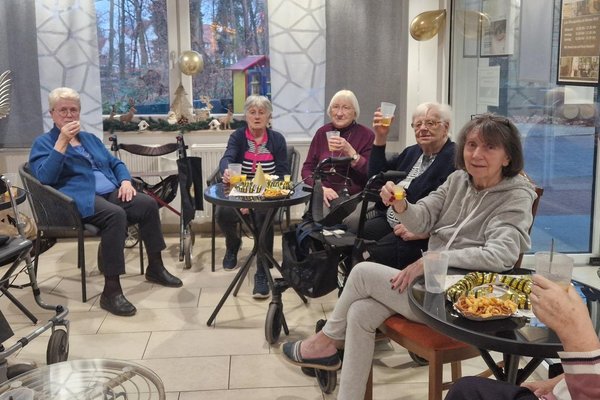 Eine Gruppe von Seniorinnen sitzt im Kreis und prostet mit ihren Getränken