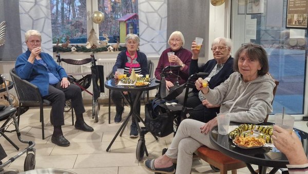 Eine Gruppe von Seniorinnen sitzt im Kreis und prostet mit ihren Getränken