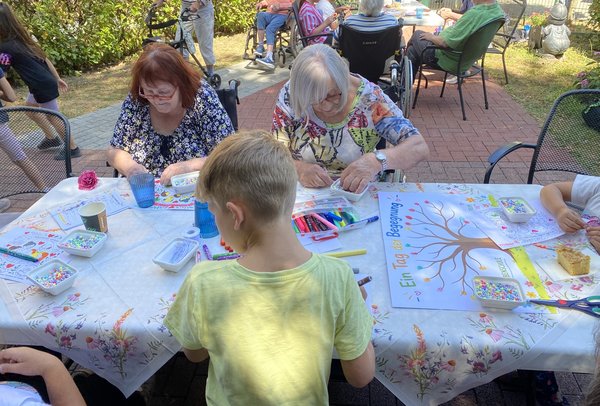 Zwei Seniorinnen und ein Junge sitzen an einem Tisch und basteln gemeinsam.