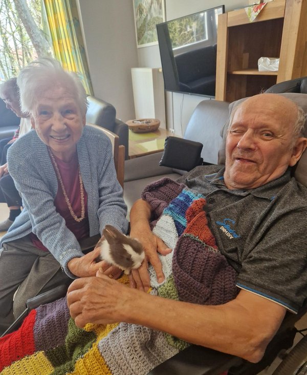 Älteres Ehepaar lächelt, während die Frau ein Kaninchen auf dem Arm hält.