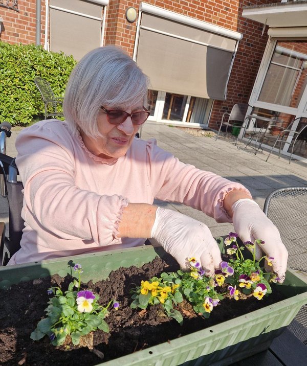 Eine Frau bepflanzt im Sitzen einen Blumenkasten.