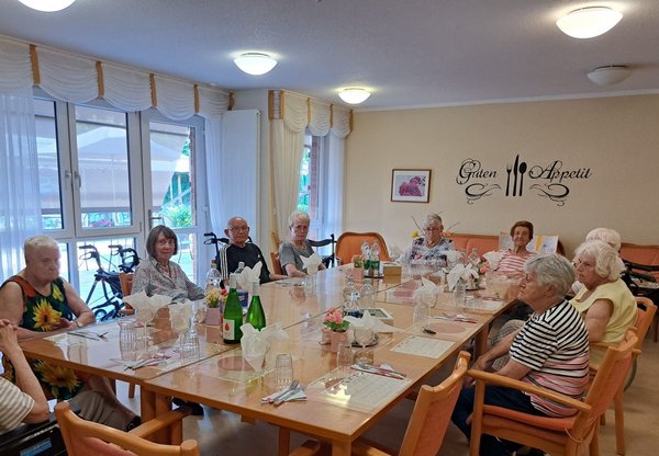 Mehrere Seniorinnen und Senioren sitzen gemeinsam an einer festlich gedeckten Tafel und genießen einen geselligen Abend