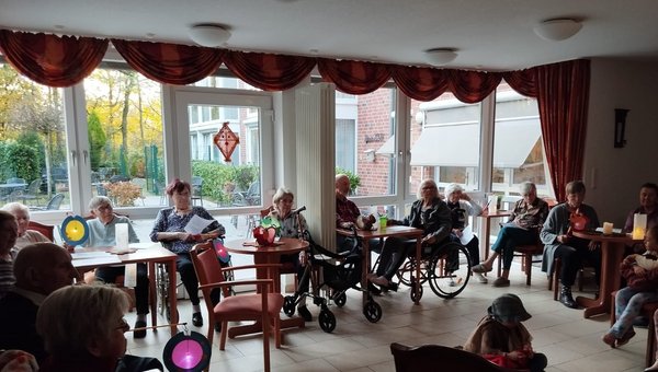 Man sieht eine Gruppe von Senioren in einem großen Kreis sitzen, sie halten St.-Martins-Laternen in ihren Händen.