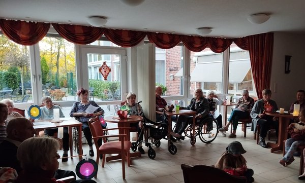 Man sieht eine Gruppe von Senioren in einem großen Kreis sitzen, sie halten St.-Martins-Laternen in ihren Händen.