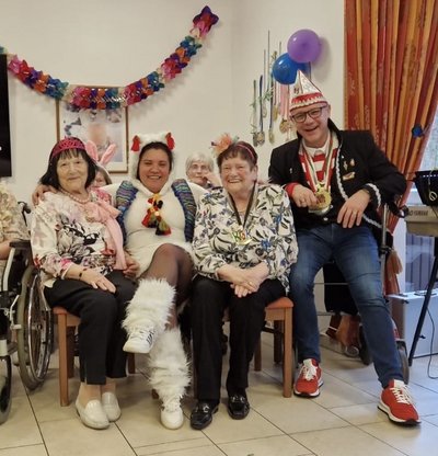 Vier Personen in bunten Karnevalskostümen sitzen nebeneinander und lachen fröhlich.