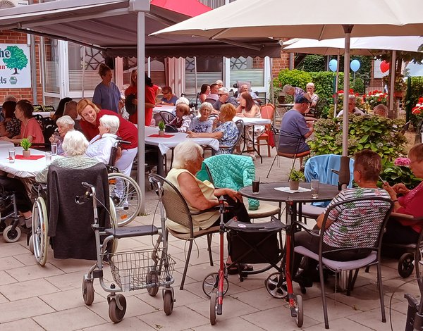 Mehrere ältere Menschen verbringen das Sommerfest gemeinsam auf der Terrasse und sitzen in kleinen Gruppen beieinander.