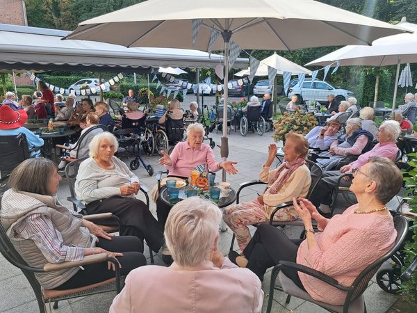 Eine bayerisch geschmückte Terrasse mit vielen Seniorinnen und Senioren, die in kleinen Gruppen zusammensitzen.