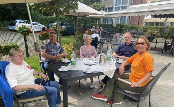 Eine Gruppe von Menschen sitzt auf der Terrasse um einen Tisch bei Kaffee und Kuchen.