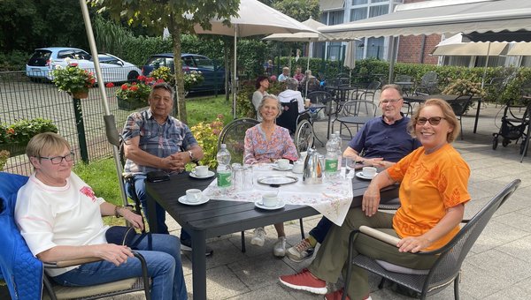 Eine Gruppe von Menschen sitzt auf der Terrasse um einen Tisch bei Kaffee und Kuchen.