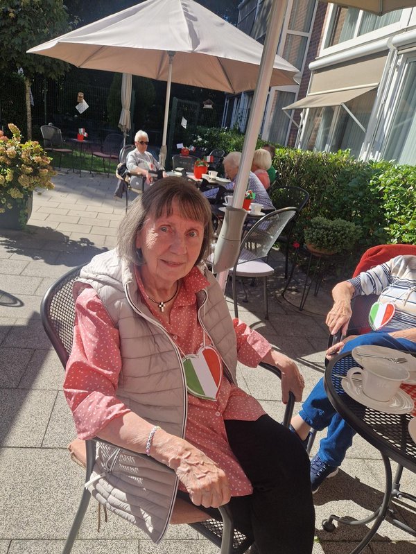 Eine Bewohnerin sitzt auf der Terrasse und trägt ein Italien-Herz um den Hals.
