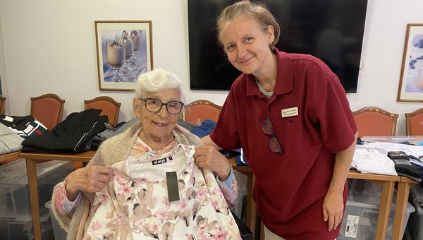 Auf dem Bild sind zwei Frauen zu sehen. Eine von ihnen hält ein Shirt vor sich. Beide lächeln in die Kamera.