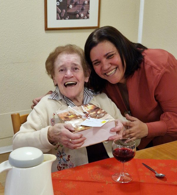 Eine Frau überreicht einem Senioren ein Geschenk, beide lachen in die Kamera.