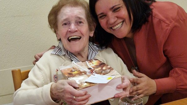 Eine Frau überreicht einem Senioren ein Geschenk, beide lachen in die Kamera.