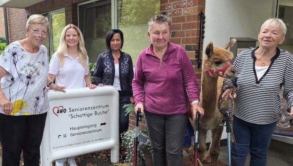 Fünf Frauen stehen vor einem Seniorenzentrum. In ihrer Mitte steht ein Alpaka.