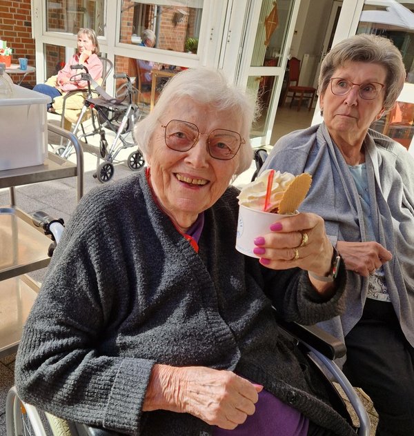 Eine Seniorin hält einen Eisbecher in der Hand und lächelt in die Kamera.