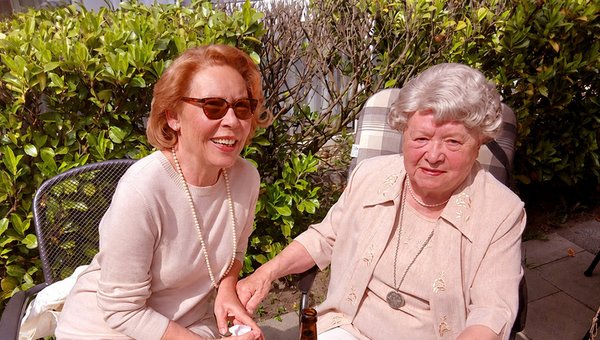 Zwei Frauen sitzen freundlich lächelnd an einem Tisch auf der Terrasse.