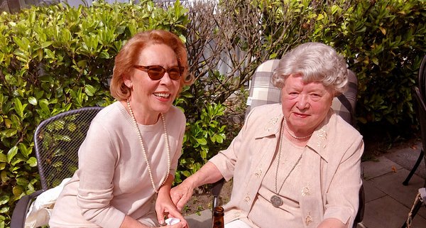 Zwei Frauen sitzen freundlich lächelnd an einem Tisch auf der Terrasse.
