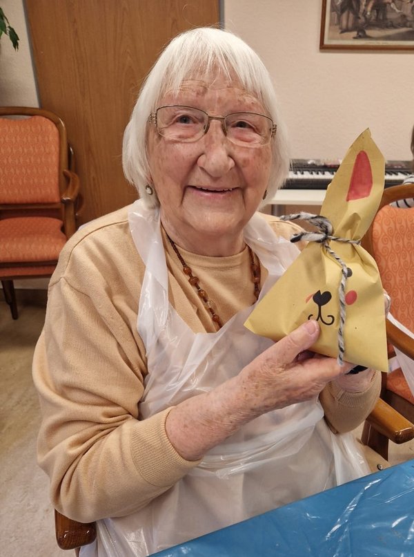 Eine Seniorin hält stolz eine selbstgebastelte Osterhasentüte in die Kamera