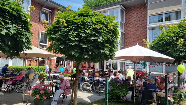 Man sieht eine geschmückte Terrasse eines Seniorenzentrums, auf der viele Senioren in kleinen Gruppen an Tischen sitzen