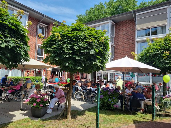 Man sieht eine geschmückte Terrasse eines Seniorenzentrums, auf der viele Senioren in kleinen Gruppen an Tischen sitzen