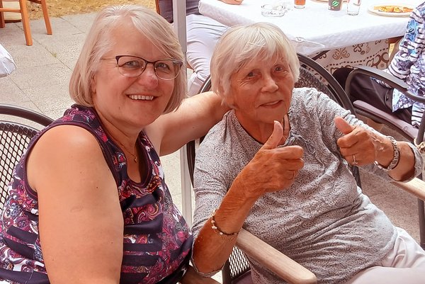 Zwei Frauen lachen in die Kamera, eine von ihnen zeigt den Daumen nach oben.