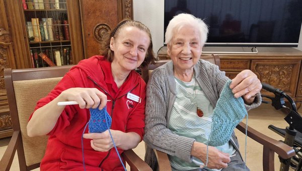 Zwei Frauen sitzen beisammen und präsentieren stolz ihre selbst gehäkelten Arbeiten.