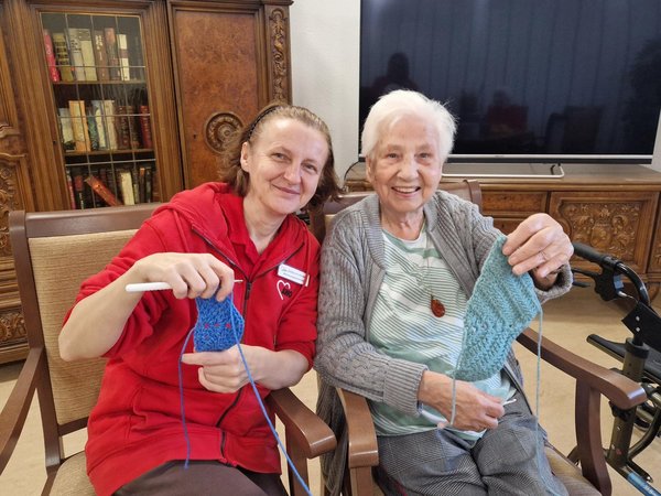 Zwei Frauen sitzen beisammen und präsentieren stolz ihre selbst gehäkelten Arbeiten.