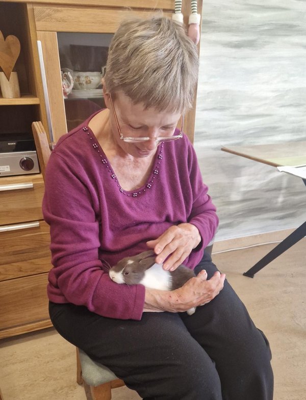 Frau lächelt und streichelt ein Kaninchen, das auf ihrem Schoß sitzt.