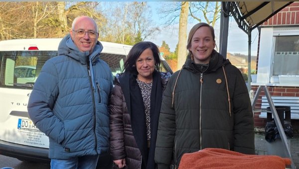 Das Bild zeigt oben zwei Frauen und einen Mann, die in die Kamera schauen. Unten ist ein Wagen mit Kartons, Tüten und Wolldecken.