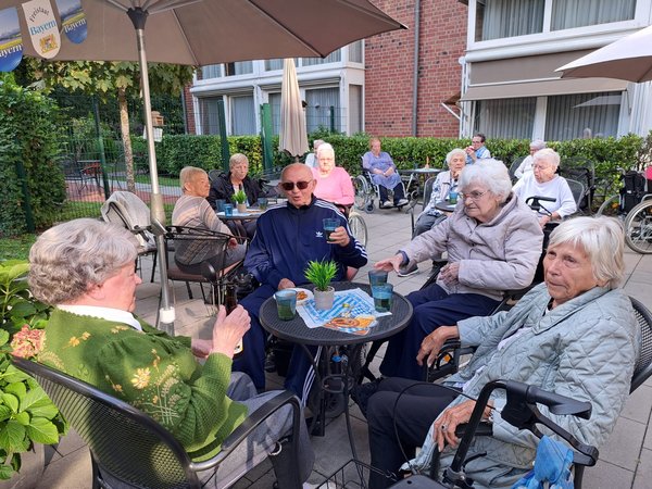 Eine Gruppe Senioren sitzt auf einer bayerisch geschmückten Terrasse.
