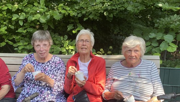 Drei Seniorinnen sitzen auf einer Bank und essen ein Eis.