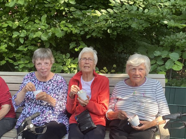 Drei Seniorinnen sitzen auf einer Bank und essen ein Eis.
