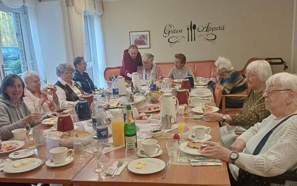 Senioren sitzen um eine reich gedeckte Ostertafel und frühstücken gemeinsam.