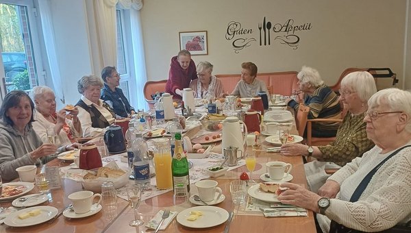 Senioren sitzen um eine reich gedeckte Ostertafel und frühstücken gemeinsam.