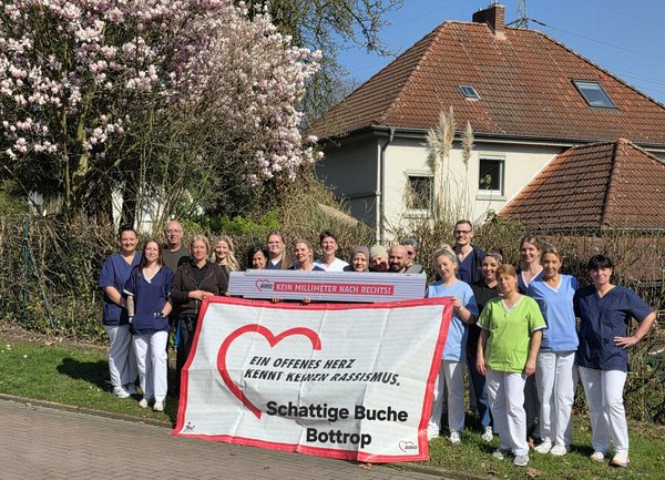 Eine Gruppe von Menschen steht um ein Plakat mit der Aufschrift "Ein offenes Herz kennt keinen Rassismus" und hält gemeinsam einen übergroßen Zollstock mit dem Text "Kein Millimeter nach rechts".