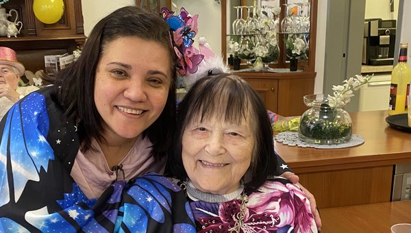 Zwei verkleidete Frauen lachen in die Kamera, eine Seniorin mit Krönchen wird von einer als Schmetterling verkleideten Frau im Arm gehalten
