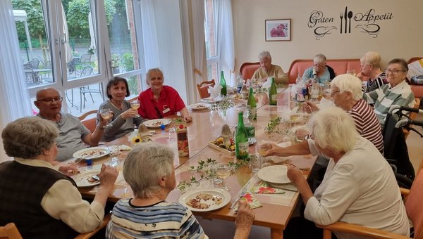 Eine Gruppe Seniorinnen und Senioren sitzt an einer großen, herbstlich dekorierten Tafel. Sie essen Flammkuchen und trinken dazu Federweißer.