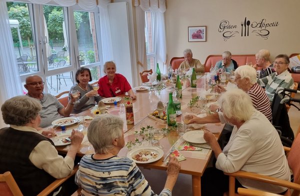 Eine Gruppe Seniorinnen und Senioren sitzt an einer großen, herbstlich dekorierten Tafel. Sie essen Flammkuchen und trinken dazu Federweißer.